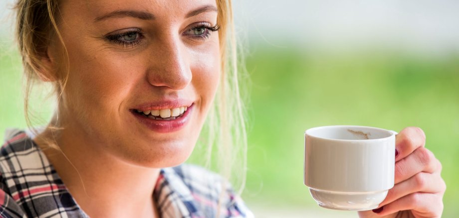 Junge Frau hält eine weiße Tasse und lächelt.