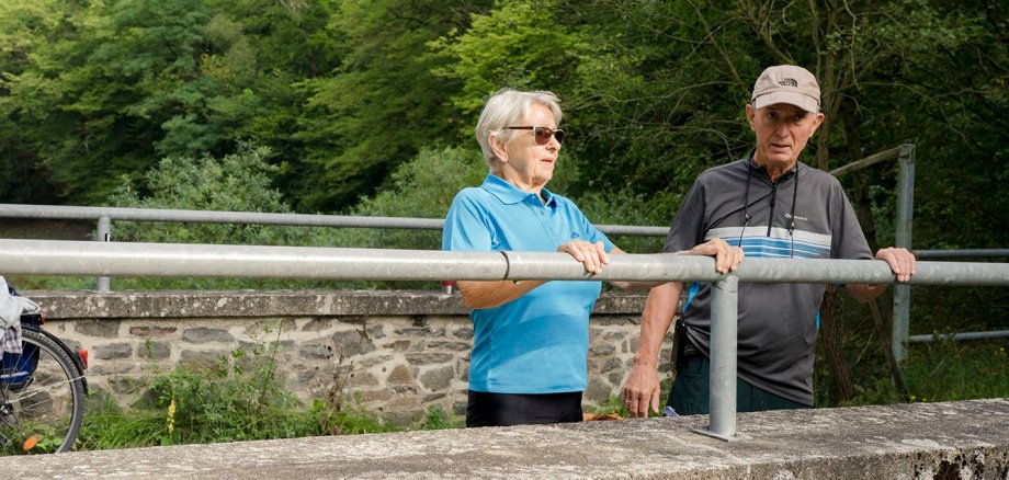 Seniorenehepaar in Fahrradkleidung steht an einem Holzgeländer