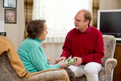 Landarzt werden Arzt im Gespräch mit einer älteren Patientin in deren Wohnzimmer
