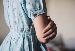 Rechtsseitige Torsoansicht eines Mädchens im hellblau geblümten Kleid mit verschränkten Armen