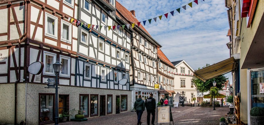 Fachwerkhäuserzeile mit Menschen auf der Straße davor und einer Fahnengirlande auf Höhe des 2. Stockwerks