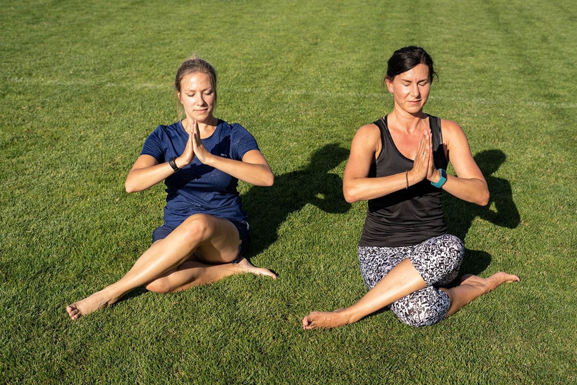 Zwei Frauen sitzen in einer Yogahaltung auf dem Rasen