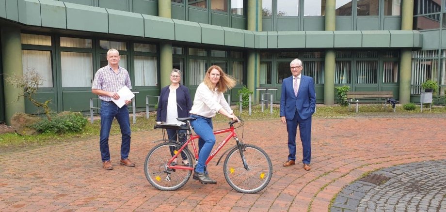 Adolf Scheuermann, Susanne Paulus, Nicole Sude und Erster Kreisbeigeordneter Karl-Friedrich Frese vor dem Kreishaus in Korbach. Frau Sude sitzt auf einem Fahrrad.