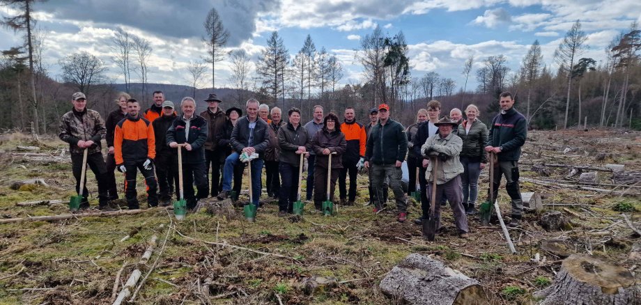 Landrat Jürgen van der Horst, Hendrik Block und die Teilnehmenden des Wild-Wald-Dialogs halten die Schippen zum Einsetzen der Baum-Setzlinge in den Händen.